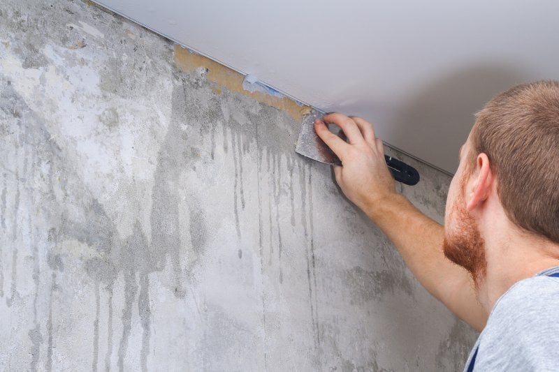 Man scraping off old wallpaper border (Photo by detry26 - stock.adobe.com)